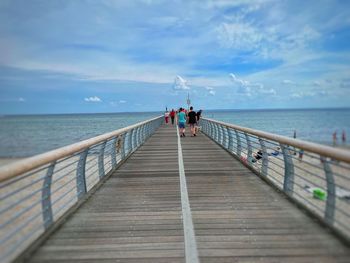 People on pier over sea against sky