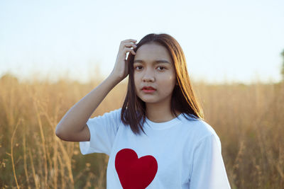 Portrait of young woman wearing sunglasses standing on field against sky