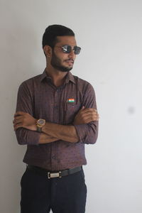 Young man wearing sunglasses standing against wall