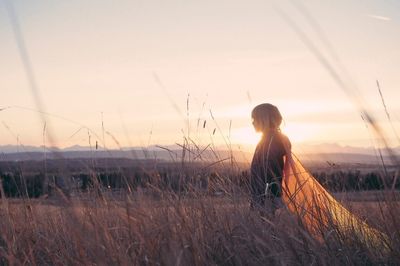 Rear view of woman on field against sky during sunset