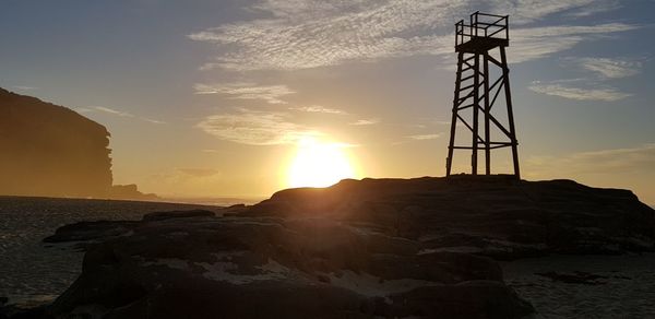 Silhouette rocks on beach against sky during sunset