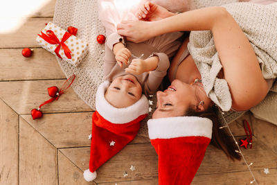 Happy family, cute mom and baby little daughter in red santa hats having fun on floor at christmas