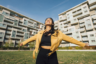 Cheerful young woman with arms outstretched standing at playground on sunny day