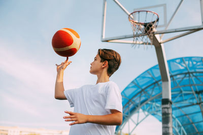 Low angle view of boy playing with basketball against sky