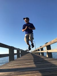 Man jumping on footbridge against clear sky