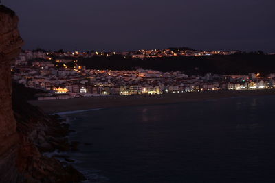 Illuminated cityscape by river against sky at night