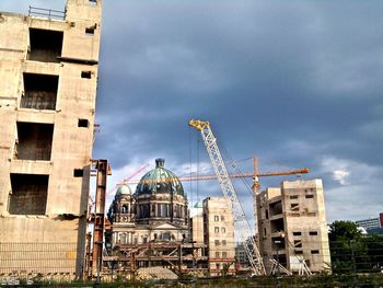 Low angle view of crane by building against sky