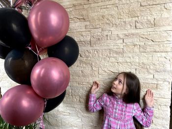 Cute girl standing by wall looking at balloon