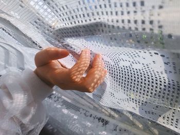 Cropped hand of woman touching white curtain at home