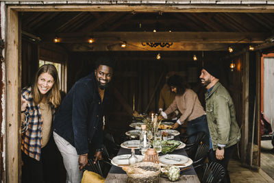 Smiling man talking to male friend while female standing by door during social gathering