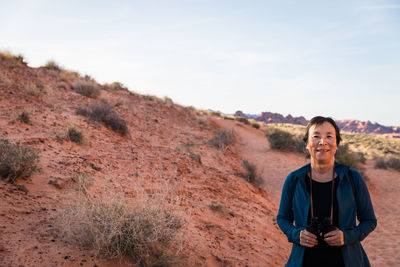 Senior asian woman smiling with binoculars in the desert landscape