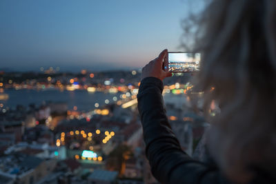 Cropped woman photographing illuminated cityscape through mobile phone at night