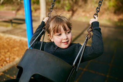 Portrait of smiling girl sitting on swing at playground