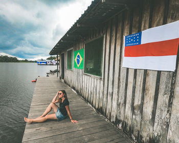 Rear view of woman sitting on pier against sky