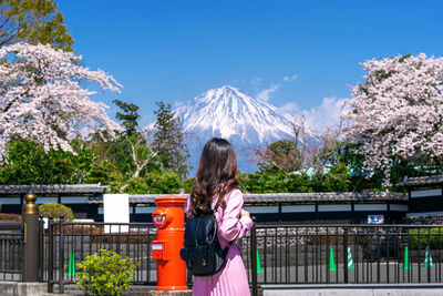 Rear view of woman standing by trees against sky