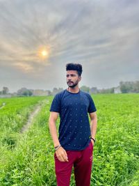 Portrait of young man standing on field against sky