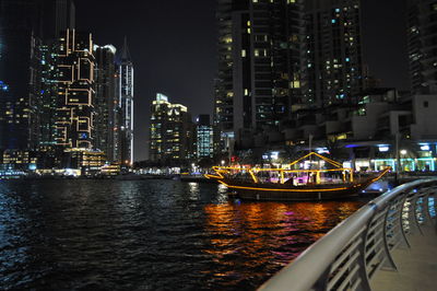 Illuminated buildings by river against sky at night