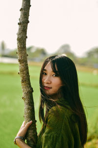 Portrait of young woman against tree trunk