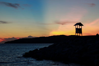 Silhouette rocks on sea against sky during sunset