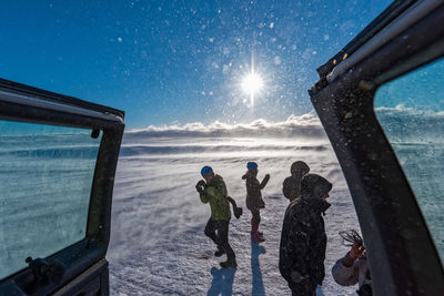 People on field during snowfall against sky