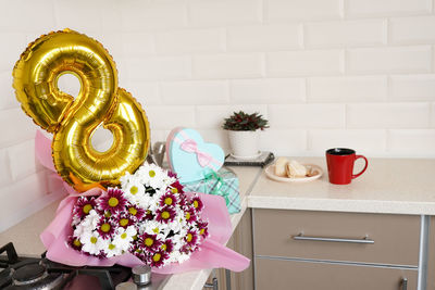 Bouquet of spring flowers and golden ballon 8 eight on kitchen table with gift box.