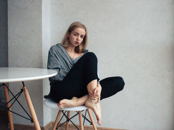 Portrait of young woman sitting on chair against wall
