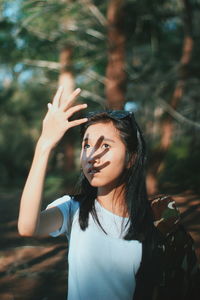 Portrait of young woman with arms raised standing against trees