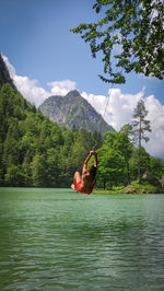 View of boy jumping in lake against sky and mountains