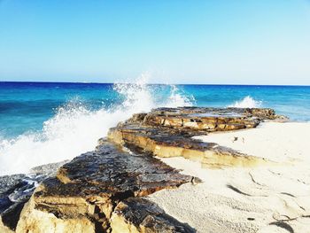 Sea waves splashing on rocks against clear sky