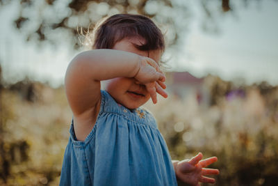 Baby girl covering face while standing outdoors