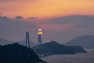 Silhouette bridge over sea against sky during sunset