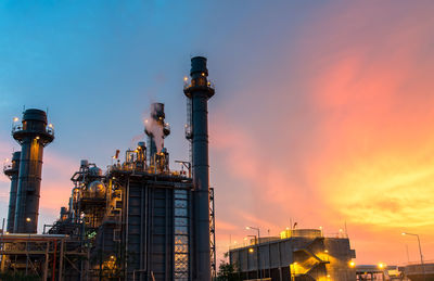 Low angle view of illuminated factory against sky during sunset