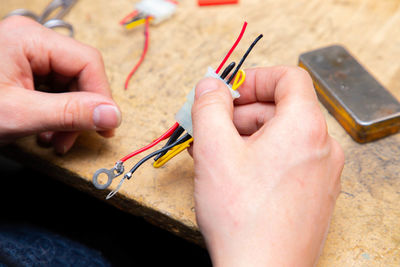 Young man's hands hold multicolored wires over desk with tools. 