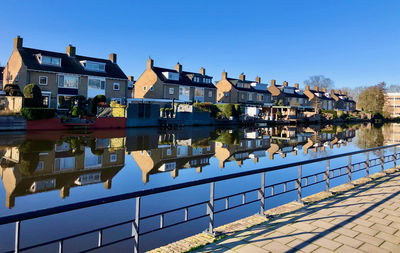 Buildings by river against clear blue sky