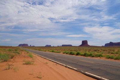 Empty road amidst field and monument valley against sky
