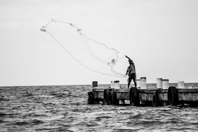 Man fishing in sea against clear sky