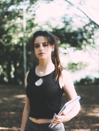 Portrait of beautiful young woman with books standing on land