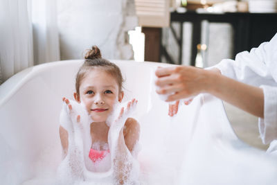 Young mother woman and little tween girl daughter having fun in the bath with foam at home