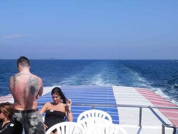 Rear view of friends standing on sea shore against clear sky