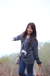 Portrait of smiling young woman standing against sky