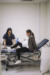 Pregnant woman sitting on gurney by doctor in medical clinic