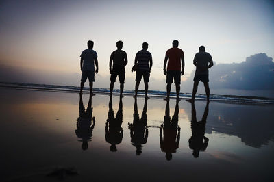 Silhouette men standing at beach against sky during sunset