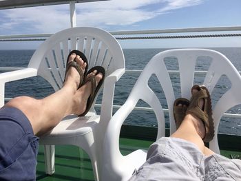 Low section of men resting on chairs in boat on sea against sky