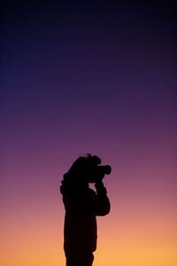 Silhouette man photographing against sky during sunset