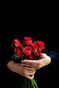 Close-up of hand holding rose bouquet against black background
