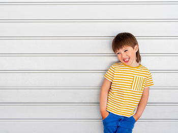 Boy on white background.kid stands hands in pockets near light grey wall.yellow shirt and blue jeans