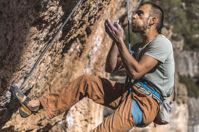 Climber talcing his hand while hanging on rope on rough cliff