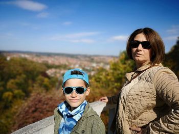 Portrait of smiling boy with mother wearing sunglasses against sky