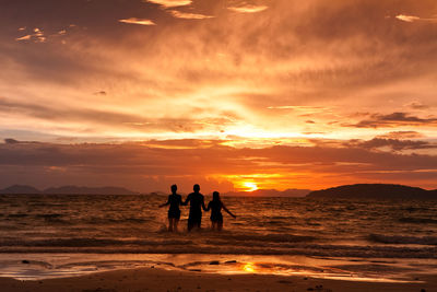 Silhouette people on beach against sky during sunset