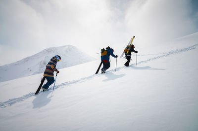 Three friends snowboarders skiers go uphill with a snowboard and skis in their hands for backcountry